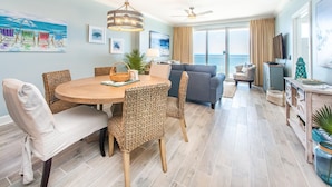A spacious living area with a round wooden table, wicker chairs, a gray sofa, and a balcony with a view. - Ocean Villa 1406 (Panama City Beach)