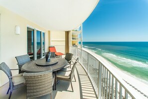 A balcony with a round table and chairs, overlooking a beach with clear blue water. - Ocean Villa 1406 (Panama City Beach)