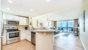 A spacious kitchen with modern appliances, a central island, and a view of the ocean through large windows. - Majestic Beach Towers 2-403 (Panama City Beach)