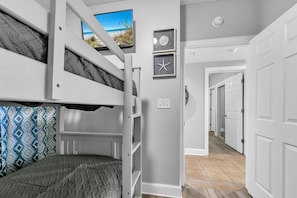 A bunk bed room with a television above it, a clock, and a door leading to another room. - Majestic Beach Towers 2-2003 (Panama City Beach)