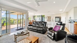 A spacious living area with a leather sofa, a coffee table, and a view of a lush garden through large sliding doors. - RidgeRaj - Kerikeri Holiday Home (Kerikeri)