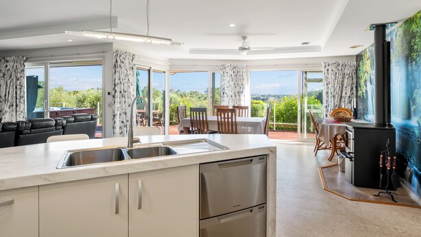 A modern kitchen with a large island, a dining area with a view, and a cozy seating area. - RidgeRaj - Kerikeri Holiday Home (Kerikeri)