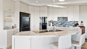 A modern kitchen with white cabinetry, a black refrigerator, a stainless steel sink, and a marble countertop. - RidgeRaj - Kerikeri Holiday Home (Kerikeri)
