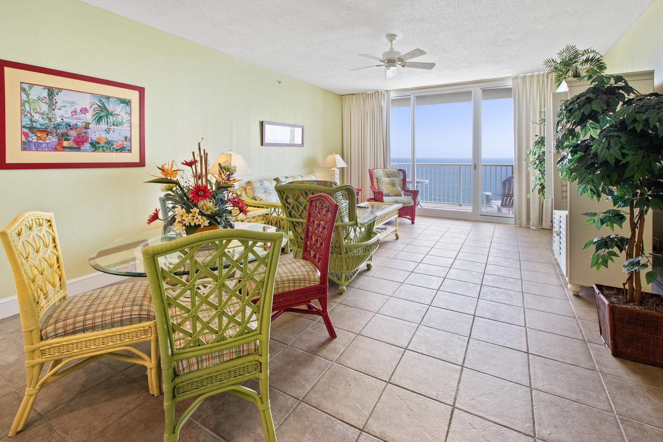 A dining area with wicker chairs and a table set for four, a ceiling fan, and a balcony with a view.