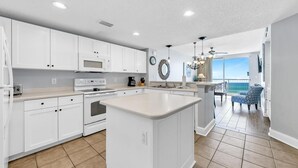 A modern kitchen with white cabinetry, a central island, and a view to a balcony. - Majestic Beach Towers 2-1206 (Panama City Beach)