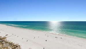 A beach with clear turquoise water, a sandy shore, and a few people walking. - Majestic Beach Towers 2-1206 (Panama City Beach)