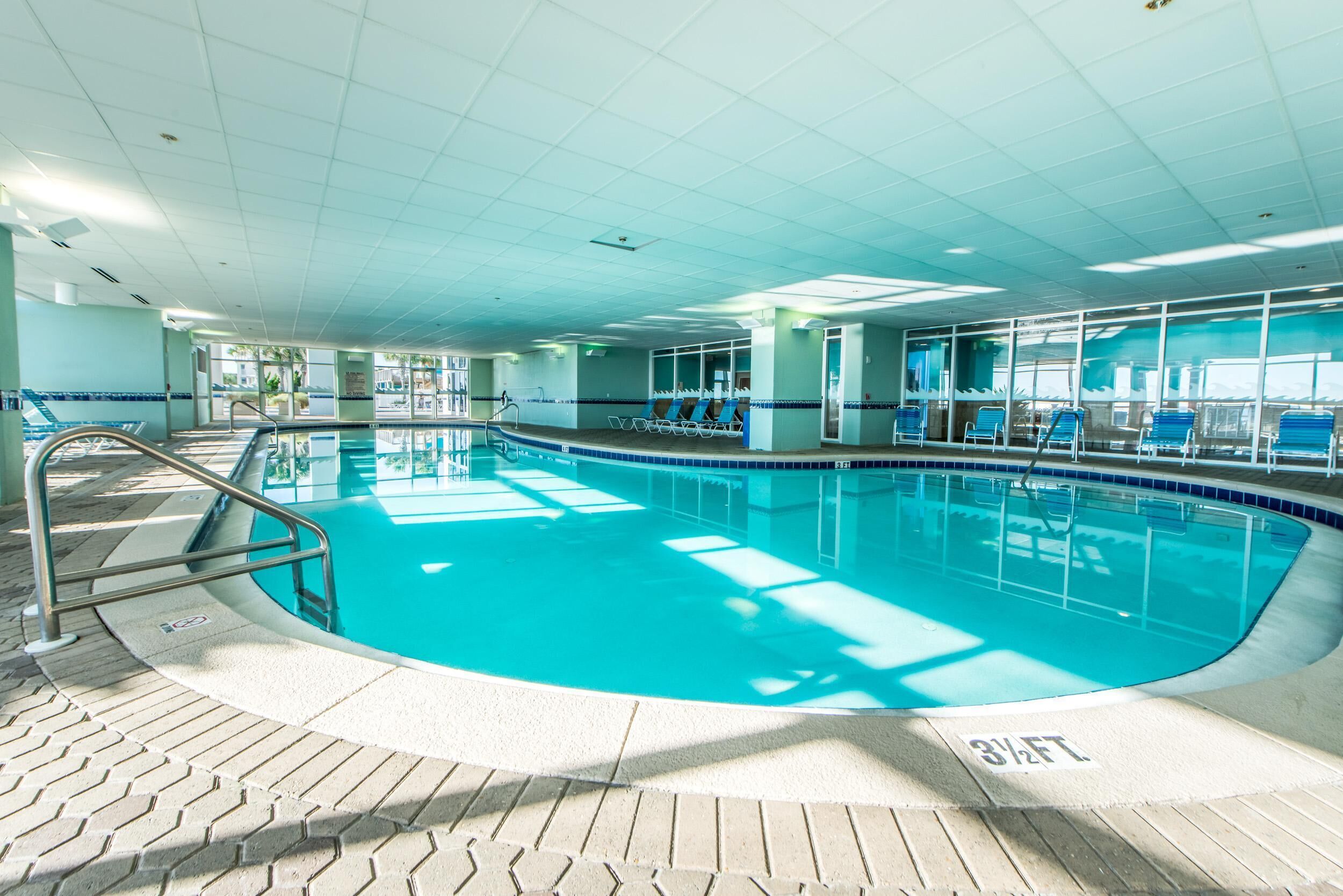 En stor inomhuspool med kristallklart blått vatten, omgiven av solstolar och en kakelbeklädd terrass.