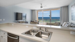 A modern kitchen with a large window, a flat-screen TV, and a dining area with a view of the ocean. - Majestic Beach Towers 1-314 (Panama City Beach)