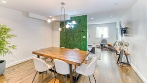 A modern dining area with a wooden table and white chairs, a green wall, and a ceiling light fixture. - Quiet DC Retreat | 3BR | Sleeps 8 (Washington)