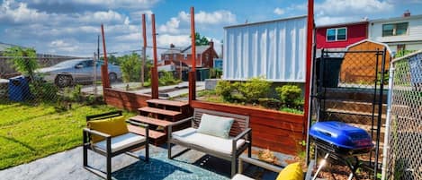 An outdoor patio with a seating area, a barbecue grill, and a fenced yard.