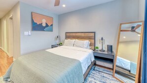 Une chambre à coucher avec un lit, une table de chevet, un miroir et un ventilateur de plafond.