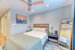 A bedroom with a bed, a nightstand, a mirror, and a ceiling fan.
