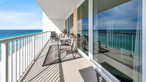 A balcony with a view of the ocean, furnished with chairs and a table, and a glass door leading to the interior. - Majestic Beach Towers 1-1803 (Panama City Beach)