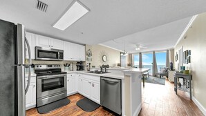 A modern kitchen with white cabinets, stainless steel appliances, and a wooden floor. - Majestic Beach Towers 1-1803 (Panama City Beach)