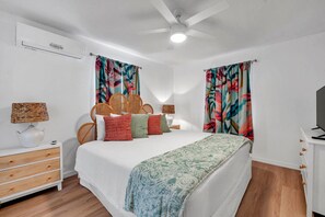 Ein Schlafzimmer mit einem Bett, zwei Nachttischen, einer Lampe, einem Fernseher und einem Deckenventilator.
