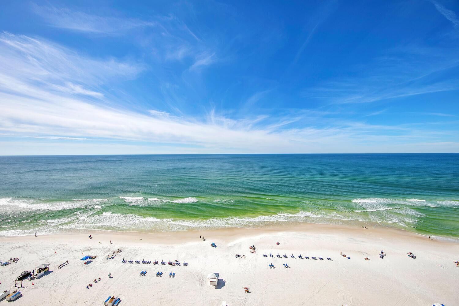 Una playa con cielos despejados, aguas tranquilas y una orilla arenosa con sombrillas y sillas de playa.