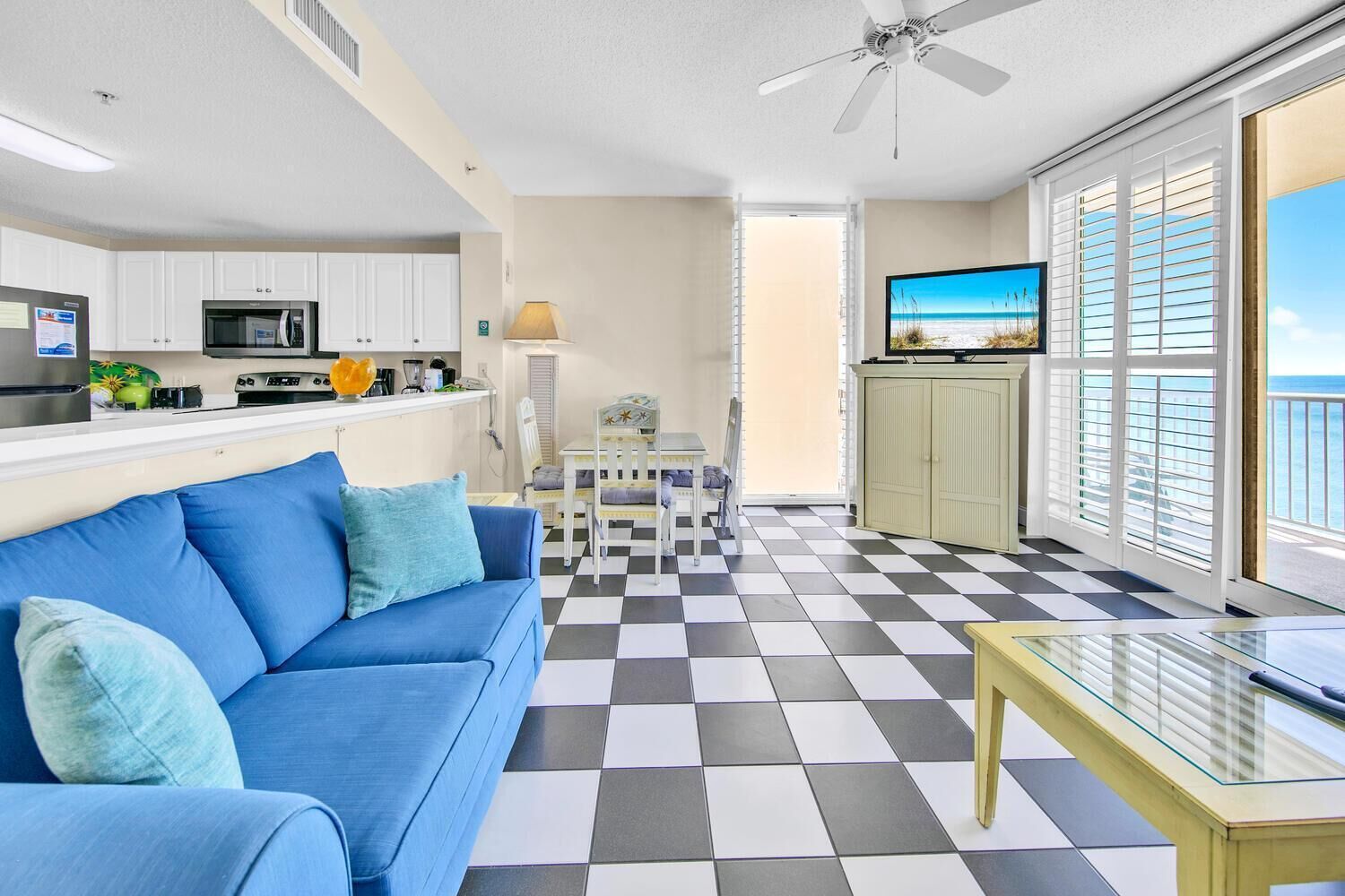 A modern living room with a blue sofa, a glass coffee table, and a checkered floor.