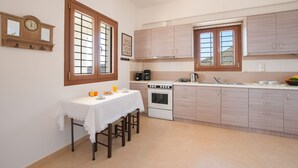A kitchen with wooden cabinets, a white countertop, a stove, and a dining table with chairs. - Angelika House -Amazing Sea view (Faistos)