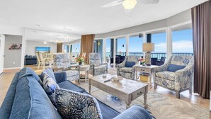 Een ruime woonkamer met een grote bank, gestreept fauteuils, een salontafel, en een balkon met uitzicht.