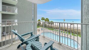 Een balkon met uitzicht op een zwembad, een zwembad en een strand op de achtergrond.