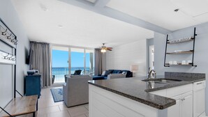 Une cuisine moderne dotée d’un grand îlot central, un coin repas avec un canapé bleu et un balcon offrant une vue dégagée.
