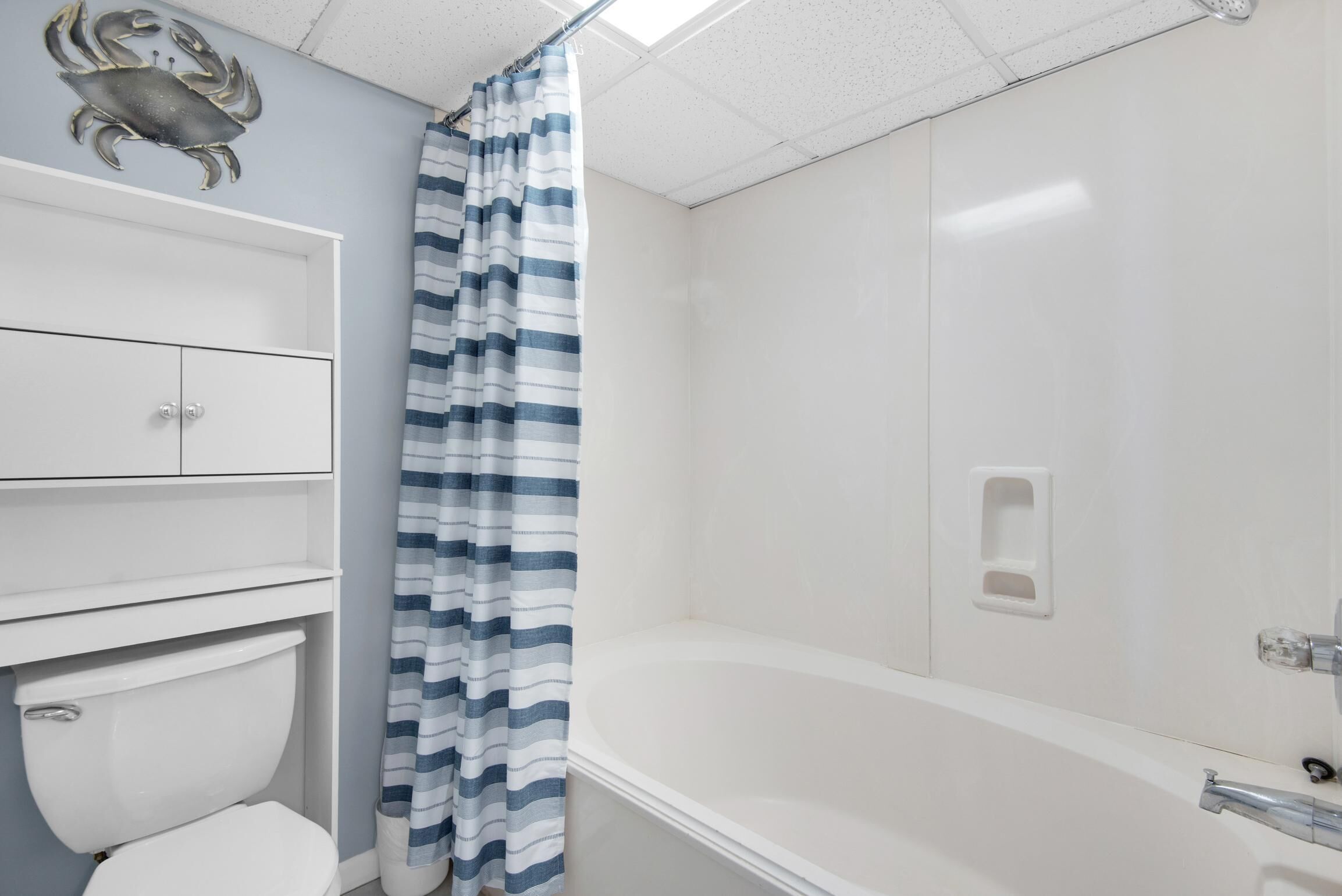 Un baño con inodoro, bañera, cortina de ducha a rayas y un cangrejo decorativo en la pared.