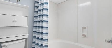 Un baño con inodoro, bañera, cortina de ducha a rayas y un cangrejo decorativo en la pared.