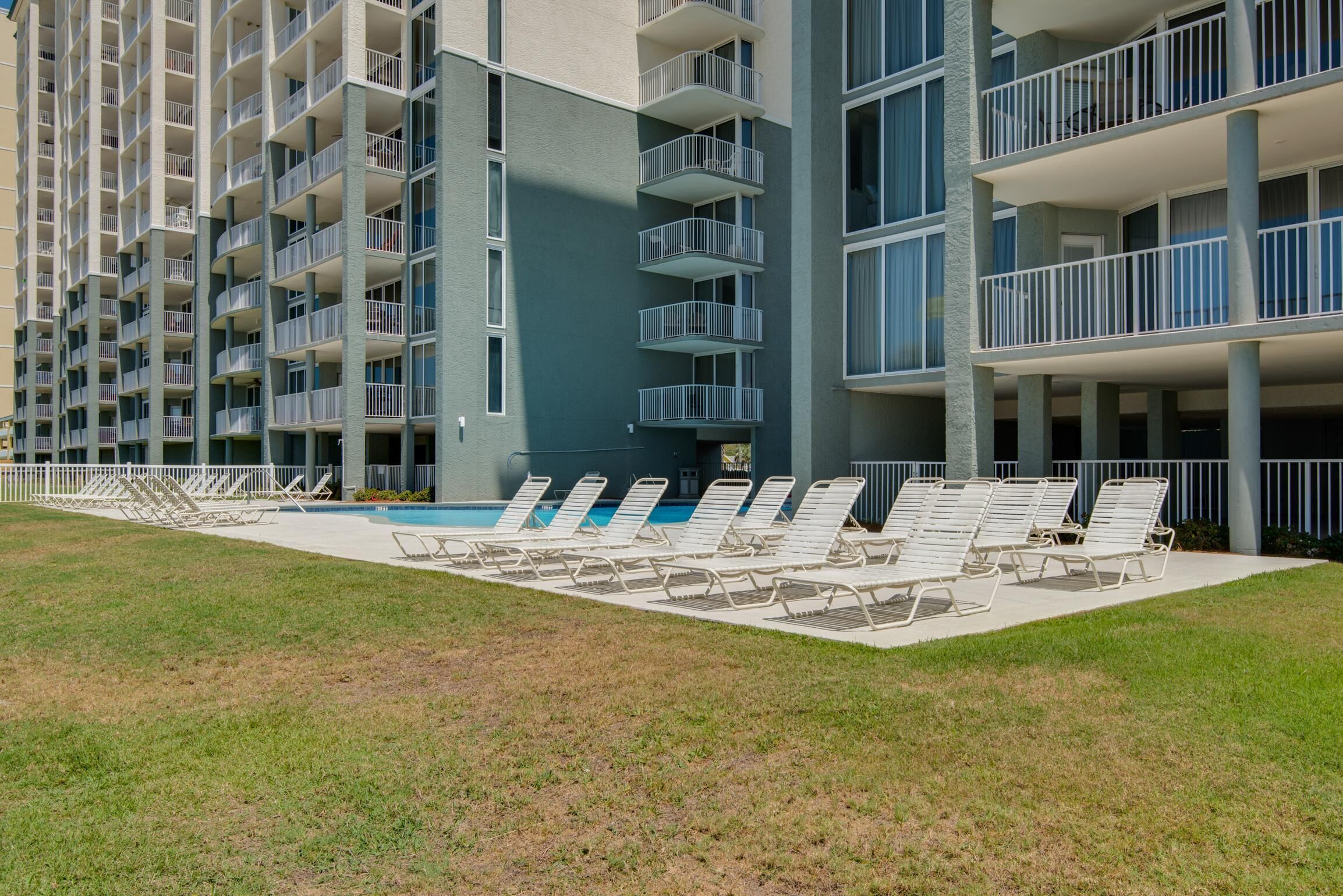A modern hotel with multiple balconies, a swimming pool, and sun loungers.