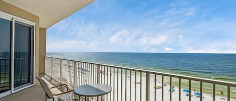 A balcony with a view of the beach, featuring a table and chairs.