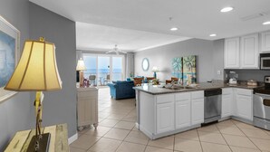 A modern kitchen with white cabinets, a central island, and a dining area with a blue sofa.