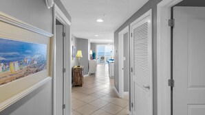 A hallway with a tiled floor, a painting on the wall, and doors leading to other rooms.