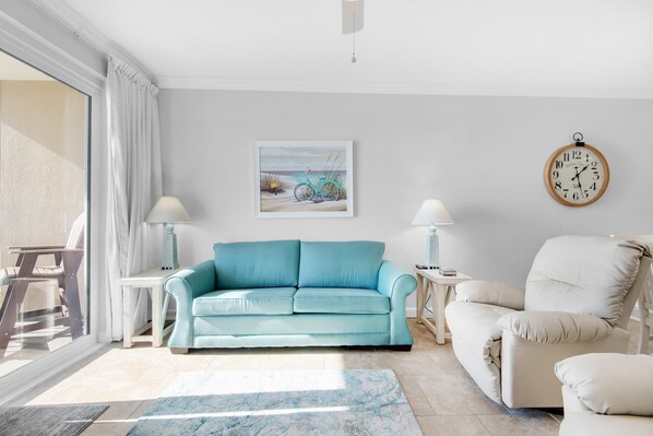Una sala de estar con un sofá azul claro, un sillón blanco, una mesita con una lámpara y un cuadro de una bicicleta en la pared.