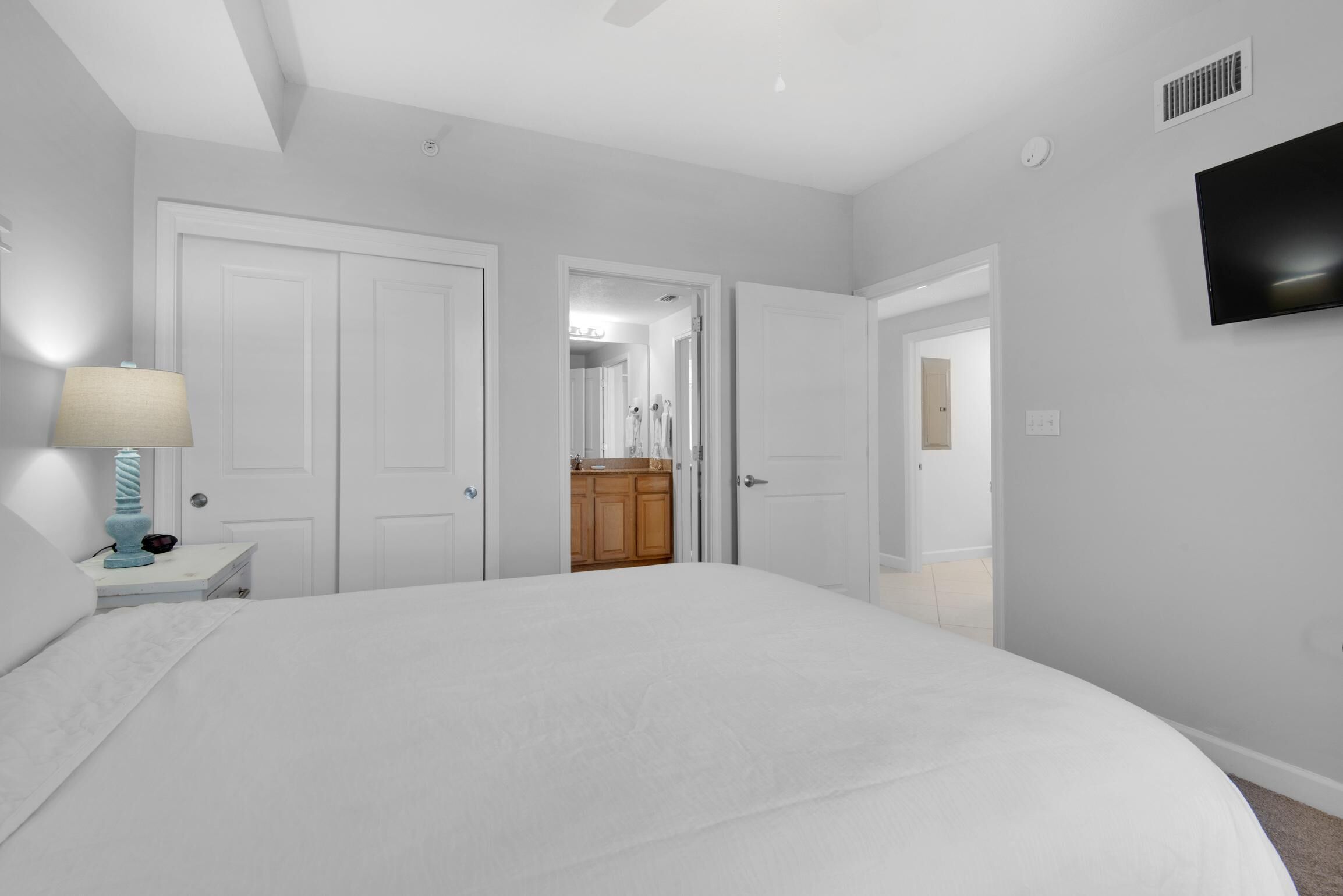 A bedroom with a large bed, a nightstand with a lamp, and a TV mounted on the wall.
