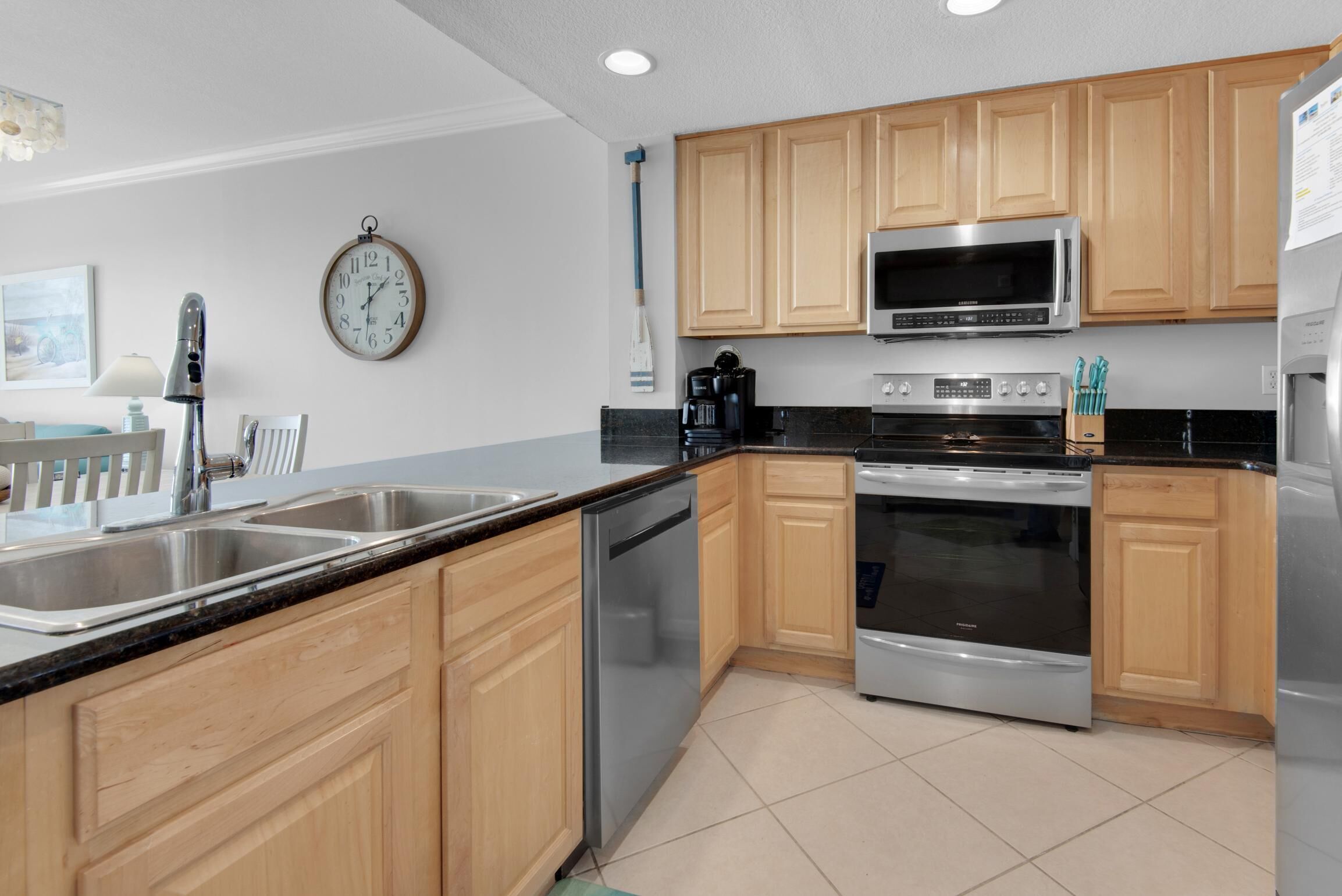 A modern kitchen with wooden cabinets, stainless steel appliances, and a large clock on the wall.