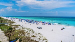 A beach with numerous umbrellas and beachgoers. - Grandview East 302 - Sandscape (Panama City Beach)