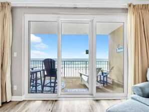 Ein Zimmer mit einer Schiebetür, die auf einen Balkon mit Blick auf den Strand führt.