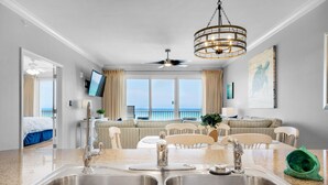 A modern kitchen with a double sink, a ceiling fan, and a view of the ocean. - Grandview East 302 - Sandscape (Panama City Beach)