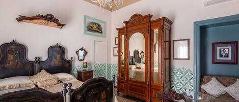A room with a large bed, a wooden wardrobe, a mirror, and a chandelier.