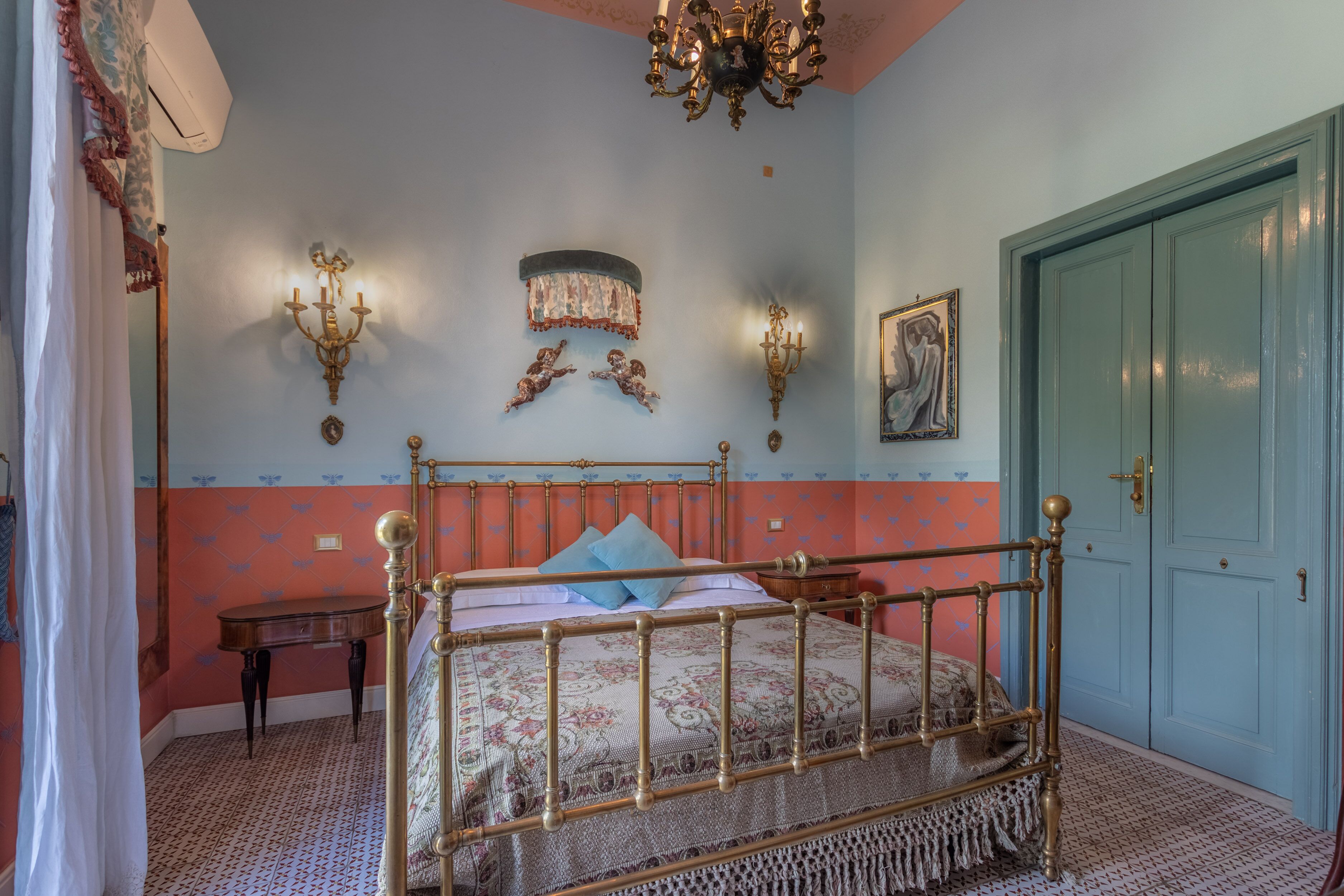 Une chambre à coucher avec un lit à baldaquin, un lustre, des appliques murales, une porte et une petite table.