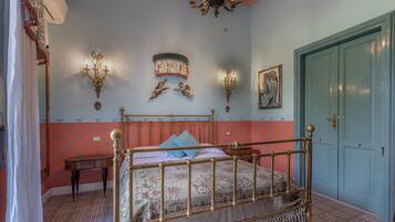 A bedroom with a four-poster bed, a chandelier, wall sconces, a door, and a small table.