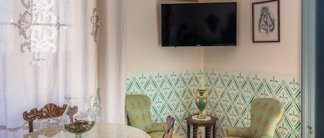 A living room with a round glass table, two patterned armchairs, a television, and a decorative vase.