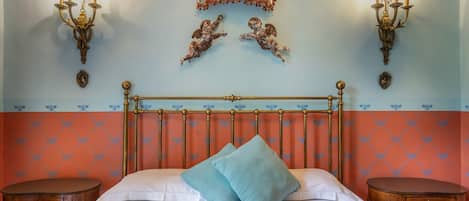 A bedroom with a bed, two nightstands, a chandelier, and wall sconces.