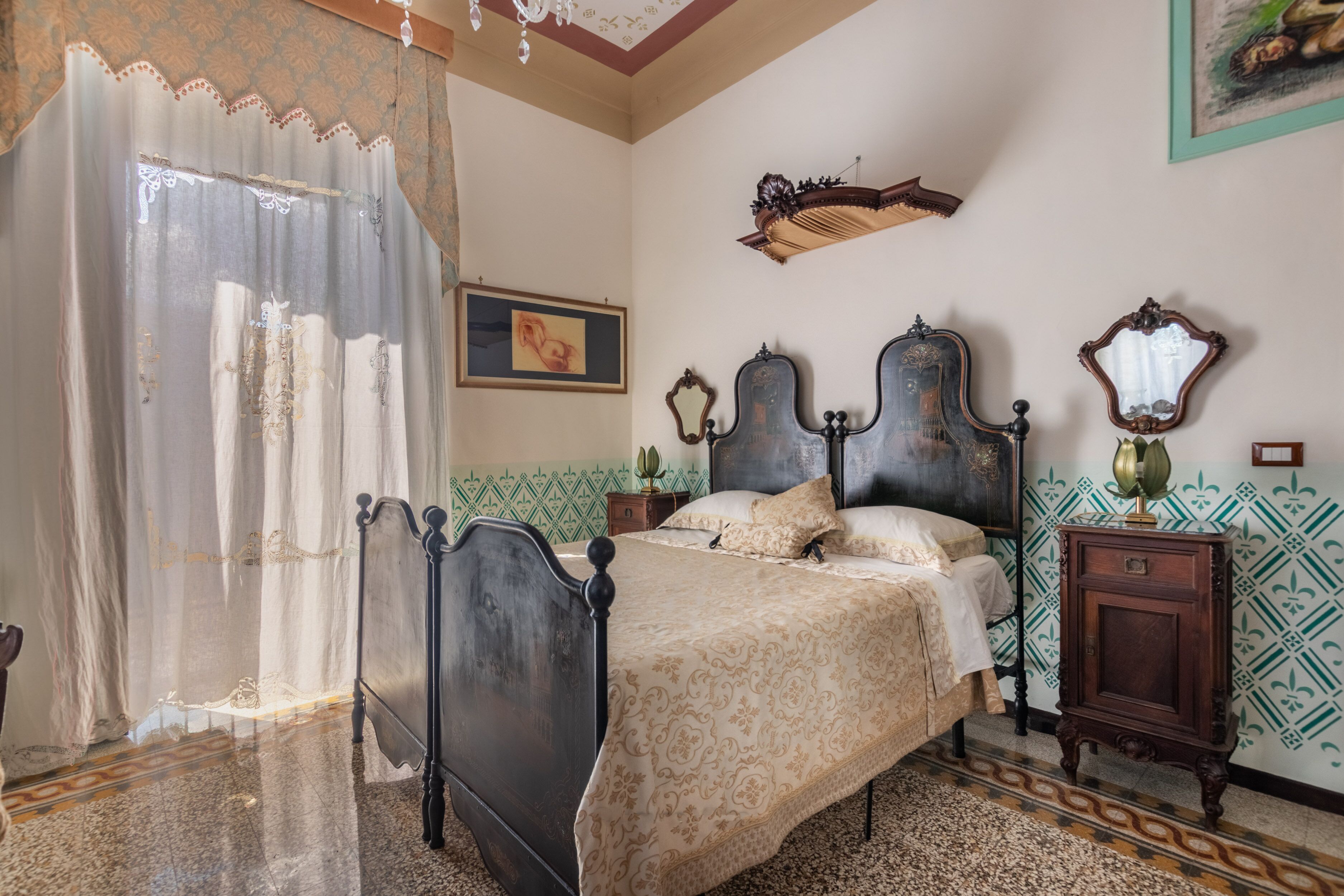 A bedroom with a bed, curtains, a nightstand, a dresser, and a wall-mounted mirror.