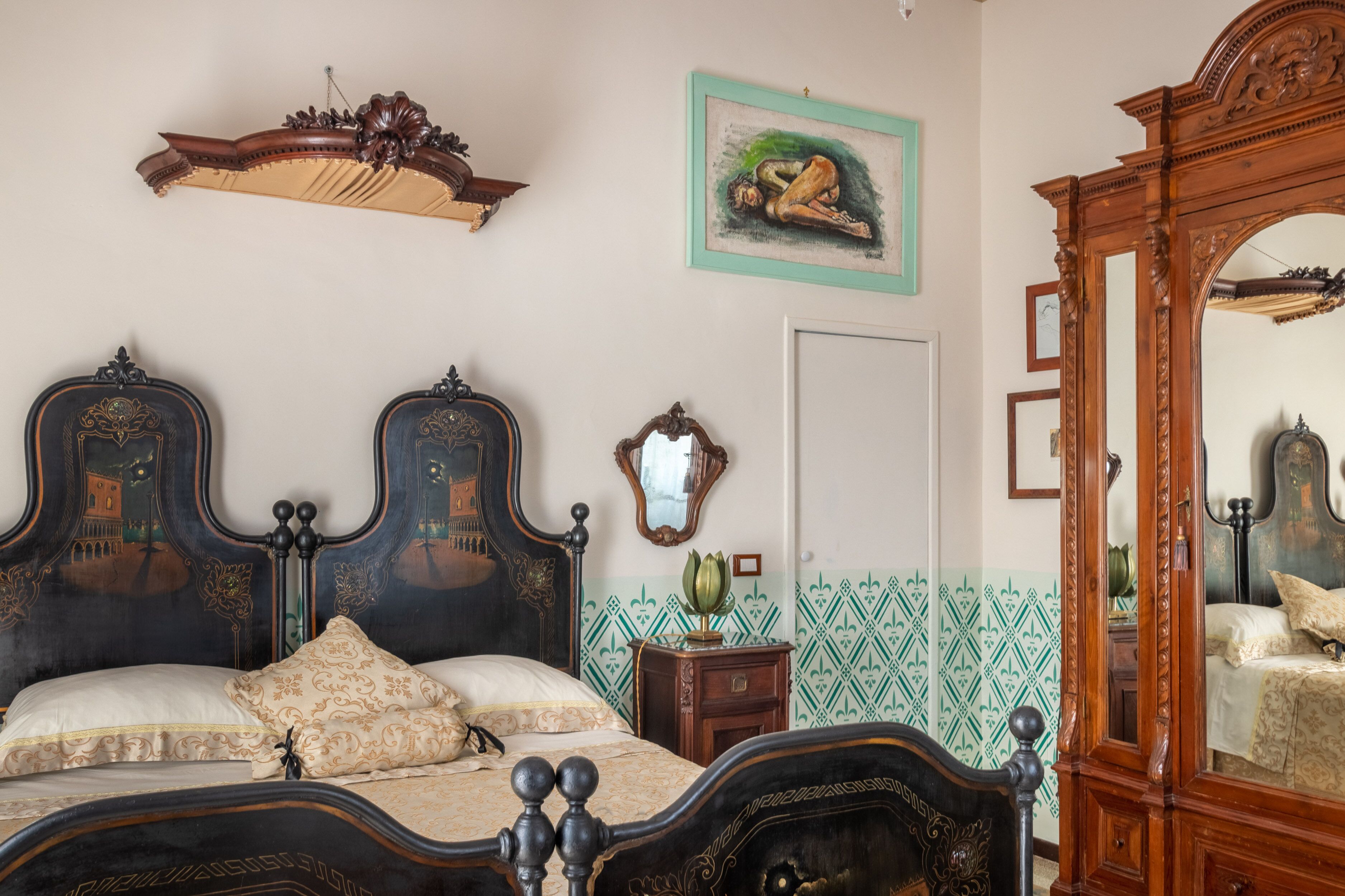 Ein Schlafzimmer mit einem großen Bett, einem verzierten Kopfteil, einem Spiegel und einer Wand mit grünem Muster.