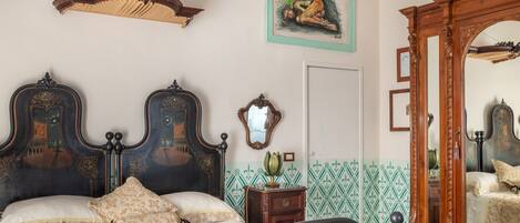Une chambre à coucher avec un grand lit, une tête de lit décorée, un miroir et un mur orné d’un motif vert.