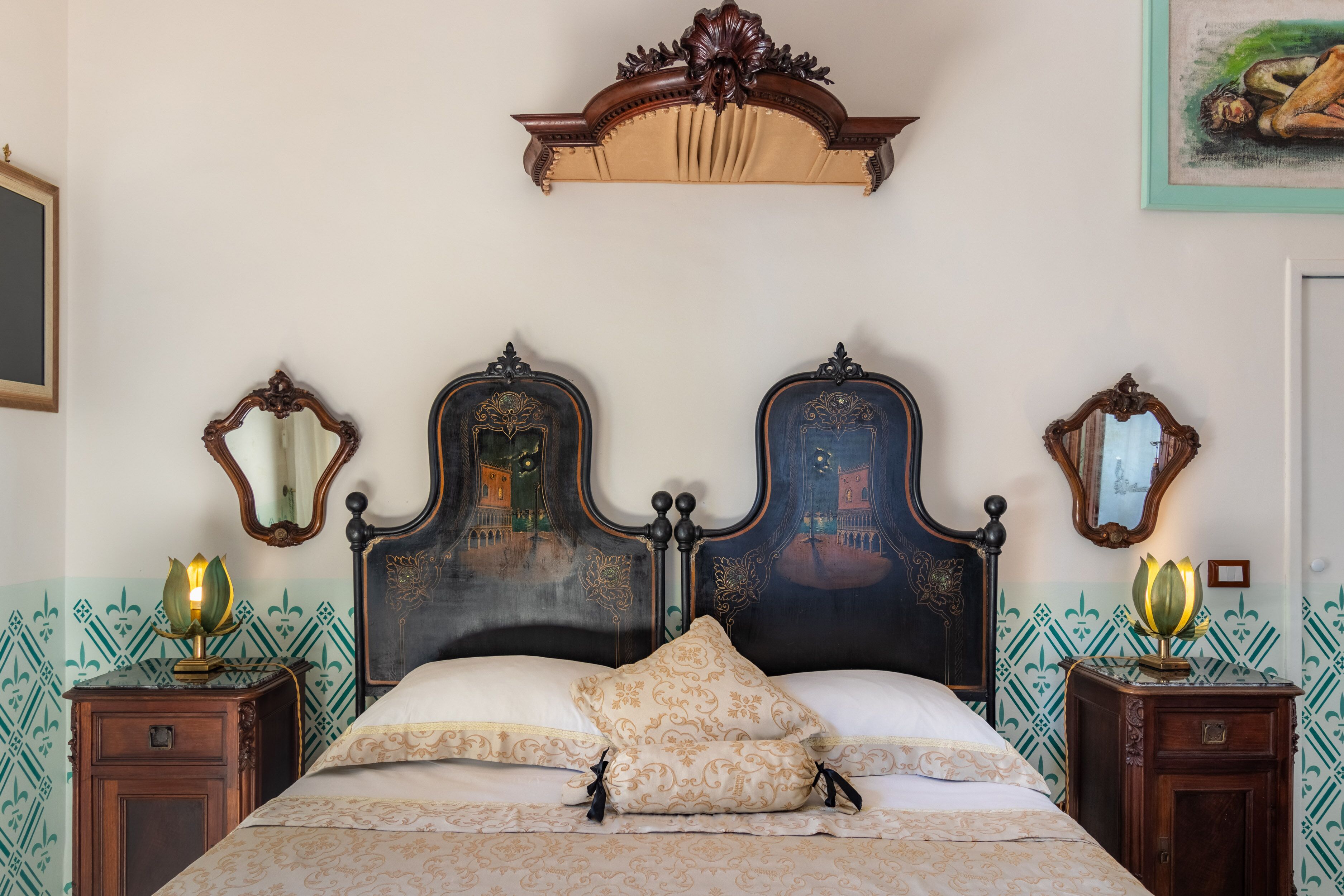 A bed with ornate headboard, two nightstands with lamps, and patterned wallpaper.