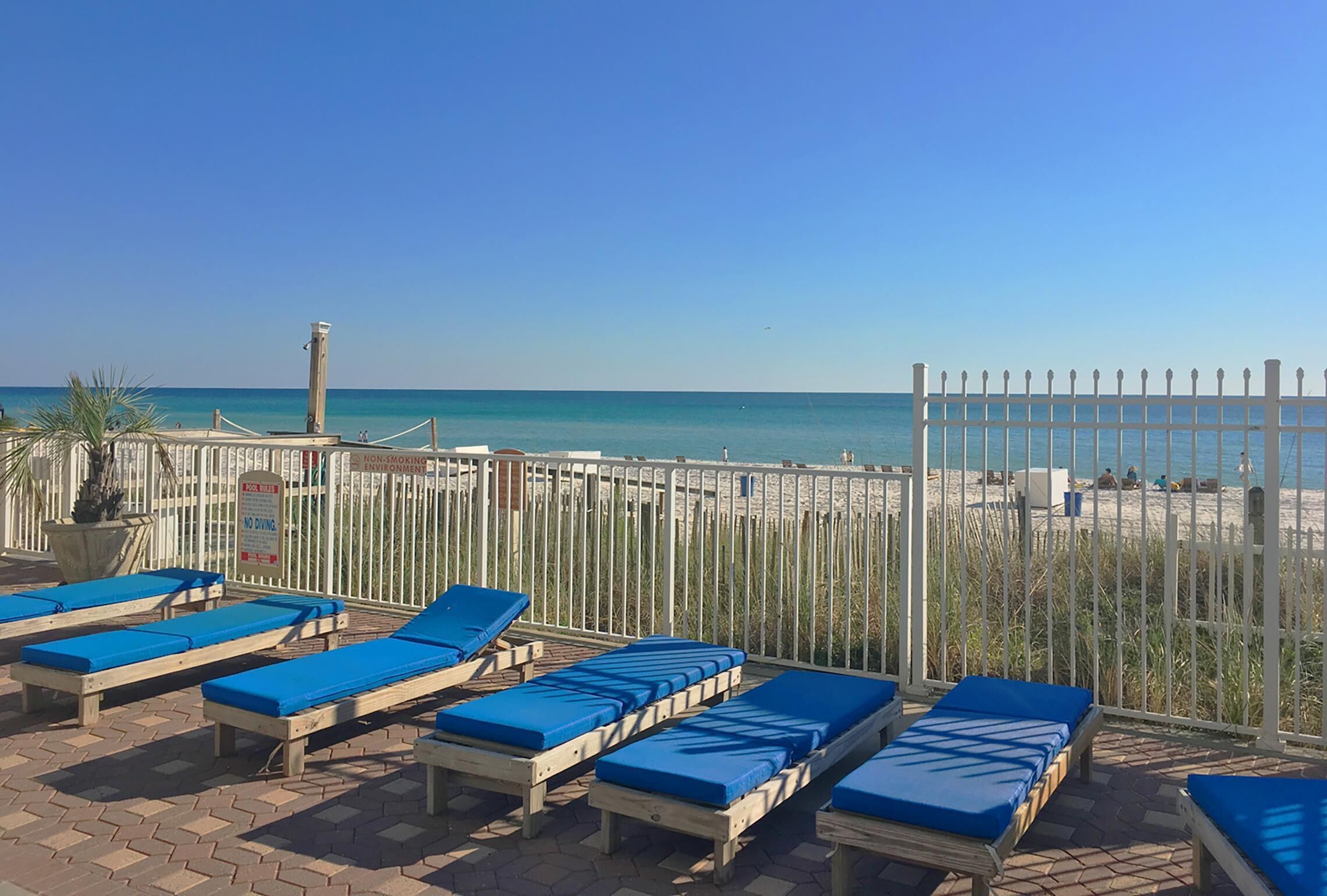 Area relax in spiaggia con lettini di legno e una recinzione bianca.