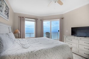 A bedroom with a large bed, a TV, and a balcony with a view of the sea.