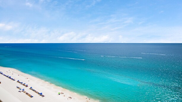 A beach with clear turquoise water, white sand, and a row of beach umbrellas. - Grandview East 1602 (Panama City Beach)