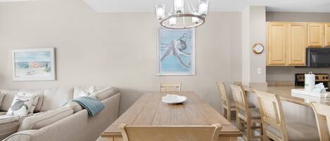 Una cocina moderna con armarios de madera, una mesa de comedor con sillas, una araña y un cuadro de un pulpo en la pared.